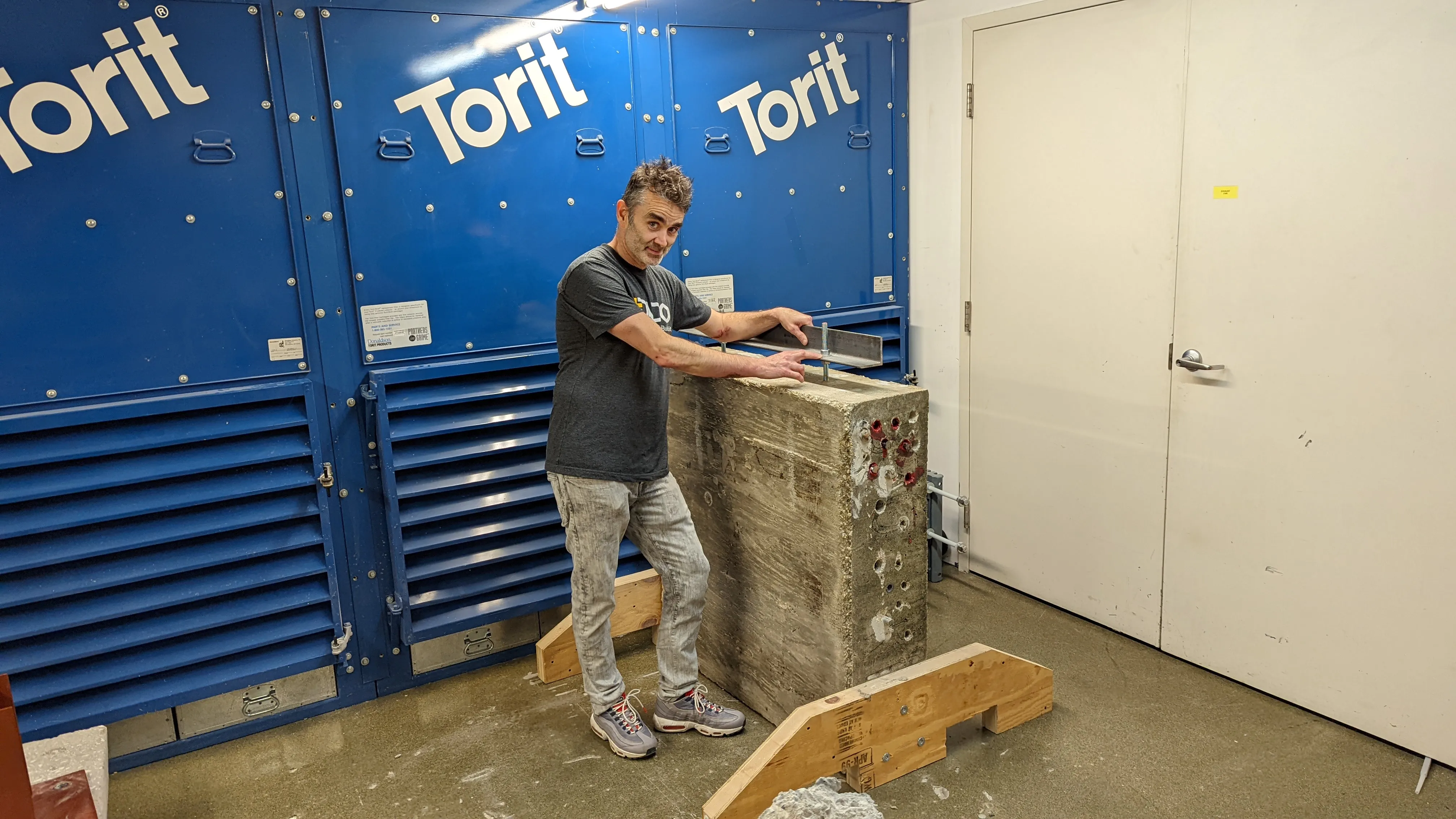 Gene Conroy-Jones in a lab standing next to a massive concrete test block during his PhD research at Cardiff University