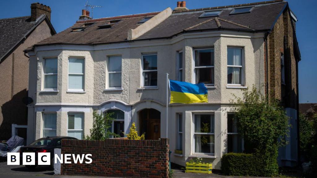 A semidetached victorian house. In the front garden a yellow and blue ukrainian flag has been erected. A window box has also been painted yellow.